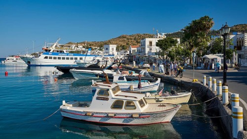 Lively harbour with many boats and white buildings surrounded by blue sea and sky, Skala, Patmos,