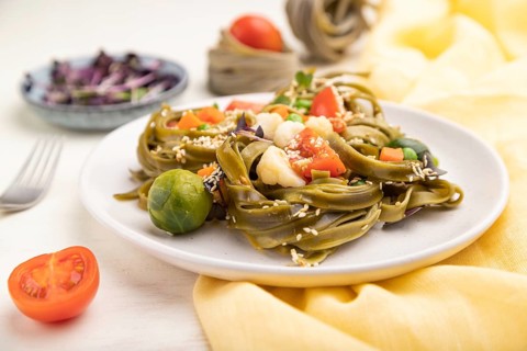 Tagliatelle green spinach pasta with tomato, pea and microgreen sprouts on a white wooden