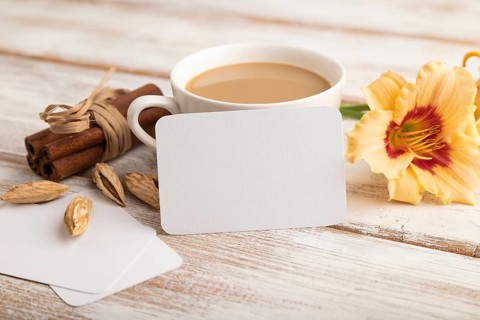 White paper business card mockup with orange day-lily flower and cup of coffee on white wooden
