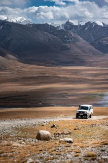 Off-road vehicle on a gravel track, glaciated and snow-covered peaks, Ak Shyrak Mountains, near