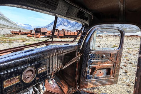 Interior view of a rusty car in front of steep mountains, remains of a US airbase from the Second