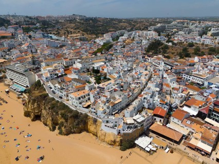 Coastal town with many white buildings on cliffs on the beach, sandy beach with bathers, aerial