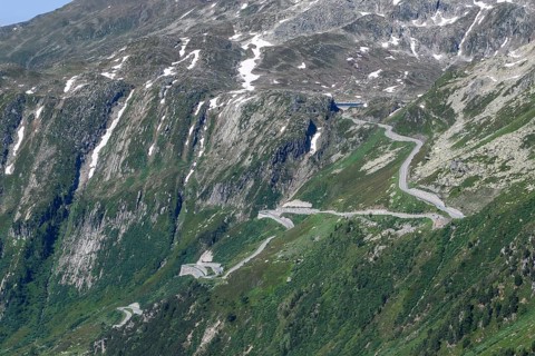 View of steep mountain road on slope above tree line with hairpin bends ascent to Grimsel Pass,
