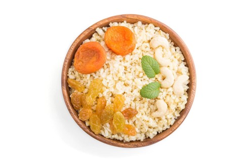 Bulgur porridge with dried apricots, raisins and cashew in wooden bowl isolated on white background