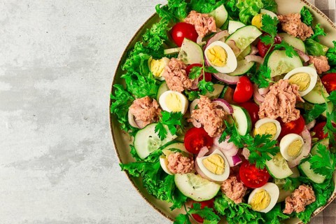 Tuna salad, vegetable salad with quail eggs, lettuce, red onion and cucumbers, on a light gray