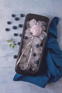 Blueberry ice cream, container with a spoon, on a gray table, fresh blueberries