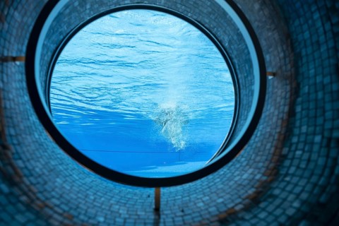 Woman Swimming in the Ship Porthole in Underwater in Swimming Pool in a Sunny Day in Switzerland