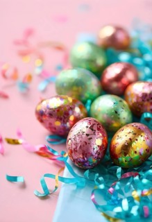 Small chocolate Easter eggs wrapped in shiny foil, placed on a bed of shredded pastel-colored