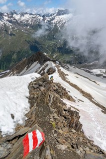 Mountaineer on a rocky ridge with snow, descent from the summit of Schönbichler Horn, view of