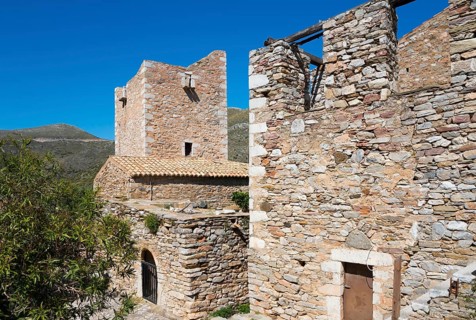 Two stone buildings of a historic village structure under a clear sky, residential towers, Vathia,