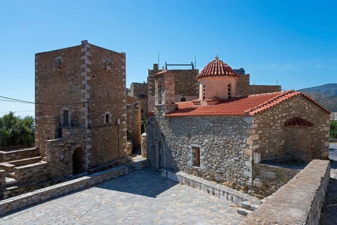 Traditional stone village buildings with red tiled roof under a blue sky, residential tower and