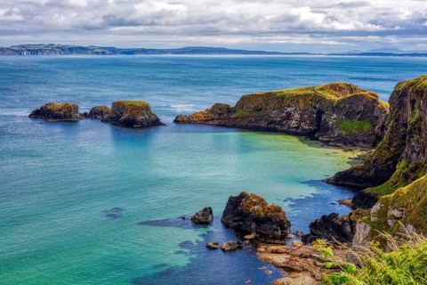 Steep cliffs overlook the clear blue-green sea under dramatic skies, County Antrim Coast