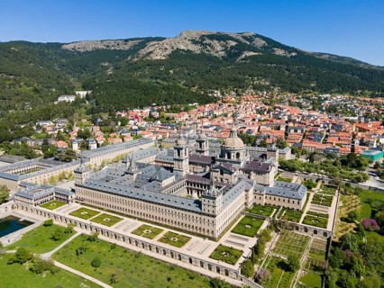 Historic monastery and neighbouring town, surrounded by green landscape and mountains, seen from