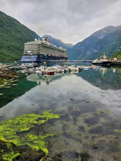 Large cruise ship, Mein Schiff 6 and boats sailing in a quiet fjord with green mountains and cloudy