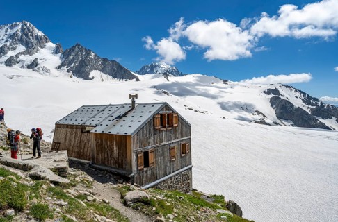Mountaineer next to a mountain hut in front of a mountain landscape, Former hut of the mountain hut