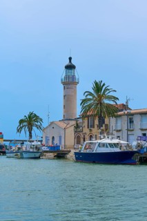 Harbour view with lighthouse, boats and palm trees in front of a clear blue sky, Le Grau-du-Roi,