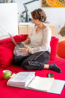 Woman, mid-50s, works from home, with laptop and communicates with colleagues via headset, home