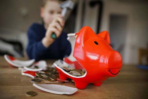 Symbolic photo on the subject of saving. A boy smashes his savings slip and counts the money it