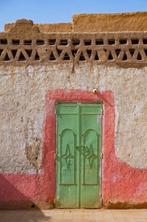 Green iron door in wall of traditional house made of mud and straw in the village Merzouga in the