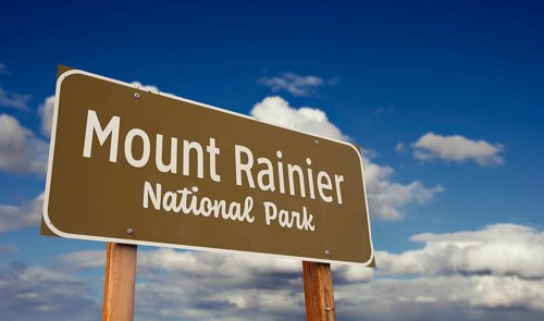 Mount rainier national park (washington) road sign against blue sky and clouds