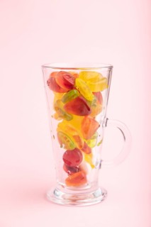 Various fruit jelly candies in drinking glass on pink pastel background. side view, close up