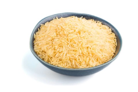 Blue ceramic bowl with raw golden rice isolated on white background. Side view, close up