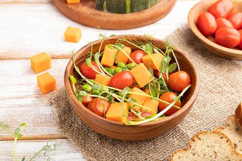 Vegetarian vegetable salad of tomatoes, pumpkin, microgreen pea sprouts on white wooden background