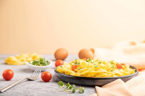 Reginelle semolina pasta with tomato, eggs and microgreen sprouts on a gray and orange background