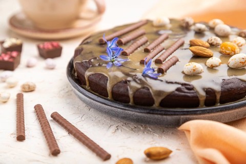 Homemade chocolate brownie cake with caramel cream and almonds with cup of coffee on a white