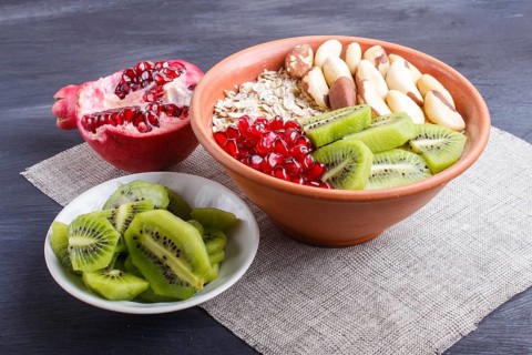A plate with muesli, kiwi, pomegranate, Brazil nuts on a black wooden background. close up