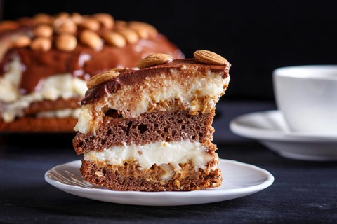 Homemade chocolate cake with milk cream, caramel and almonds on black wooden background. close up