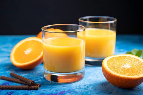 Glass of orange juice on a black and blue background. Hard light, contrast. Side view, close up