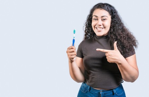 Smiling woman holding and pointing a toothbrush. Happy girl holding and pointing at toothbrush