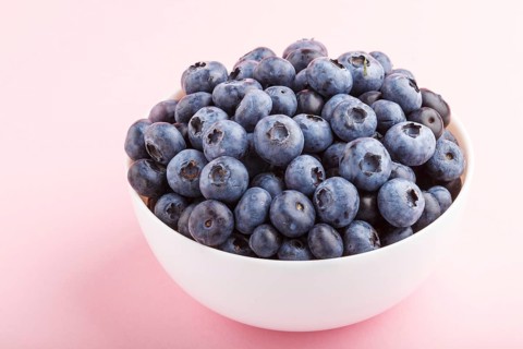 Fresh blueberry in white bowl on pink background. side view, close up