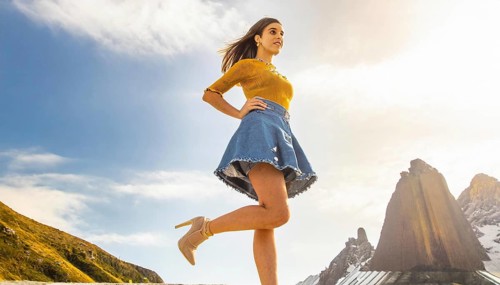 Woman walking in the mountains in sunny weather wearing a blue denim skirt and a yellow top, AI