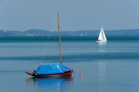 Covered and sailing boat underway on calm waters, Bernried am Starnberger See, Upper Bavaria,