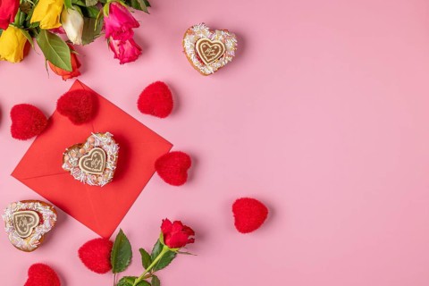 Valentine's Day composition with roses, hearts and envelope, heart-shaped cupcakes, on a pink