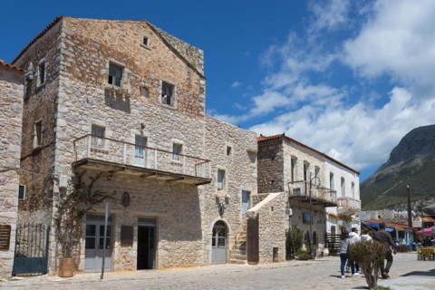 Stone buildings on a busy village street with passers-by under a blue sky with clouds, Old Town,