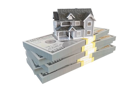 Miniature house resting on stack of thousands of dollars cash isolated on a white background