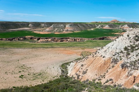 Wide valley with green meadows and dry rocks under a clear sky, Bardenas Reales Natural Park,