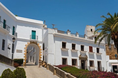 Architectural view with white buildings and a stone archway under sunshine, Arco de la Villa, Plaza
