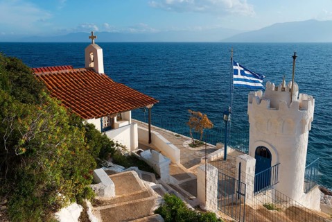 Small chapel on the coast with a view of the sea and a Greek flag, Church of Agios Nikolaos