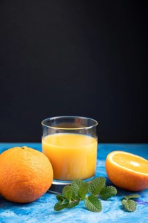 Glass of orange juice with mint on a black and blue background. Hard light, contrast. Side view,
