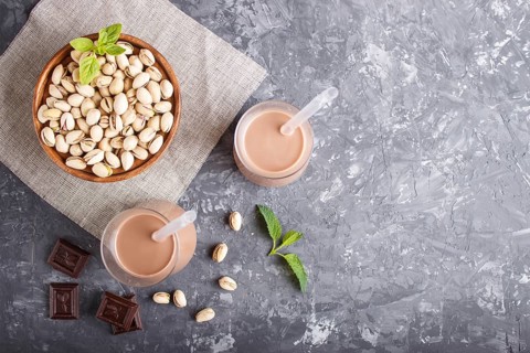Organic non dairy pistachio milk in glass and wooden plate with pistachionuts on a black concrete