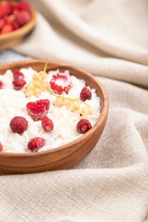 Rice flakes porridge with milk and strawberry in wooden bowl on gray wooden background and linen