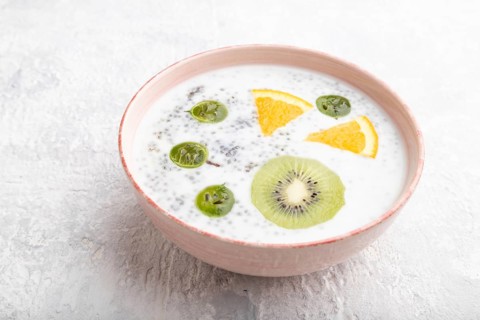 Yogurt with kiwi, gooseberry, chia in ceramic bowl on gray concrete background. Side view, close up