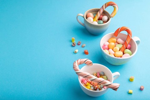 Heap of multicolored caramel candies in cups on blue pastel background. copy space, side view