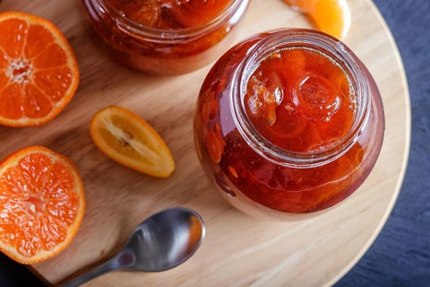 Tangerine and kumquat jam in a glass jar with fresh fruits on a black wooden table. Homemade, close
