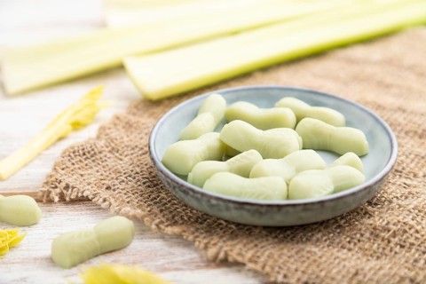 Jelly celery candies on white wooden background and linen textile. close up, side view, selective