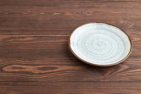 Empty blue ceramic plate on brown wooden background. Side view, copy space